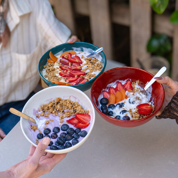 Granola ve meyveyle doldurulmuş iki stoneware bowl elde tutuluyor
